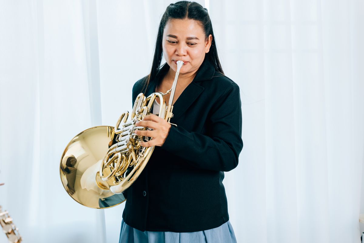 A woman playing the french horn standing up at home